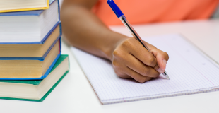 Woman in orange shirt writing in notebook next to stack of books